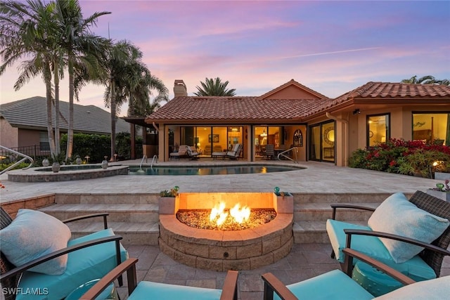 patio terrace at dusk with an outdoor fire pit, an in-ground hot tub, and an outdoor pool