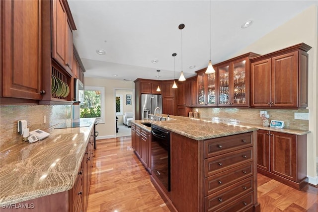 kitchen featuring black appliances, a kitchen island with sink, light stone counters, tasteful backsplash, and light wood-style flooring