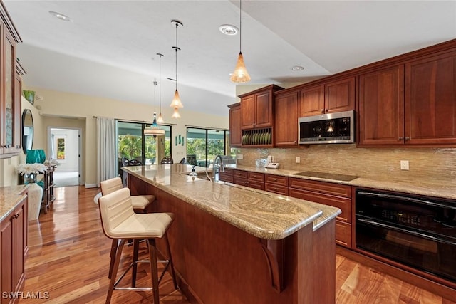 kitchen featuring black appliances, tasteful backsplash, a kitchen breakfast bar, light wood-type flooring, and light stone counters