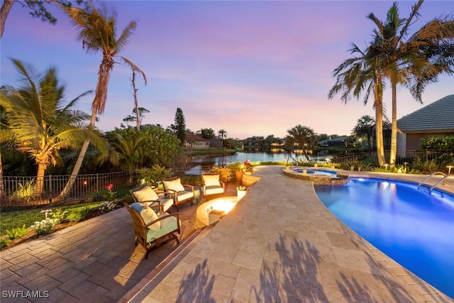 pool at dusk with a patio area, a water view, fence, and a pool with connected hot tub
