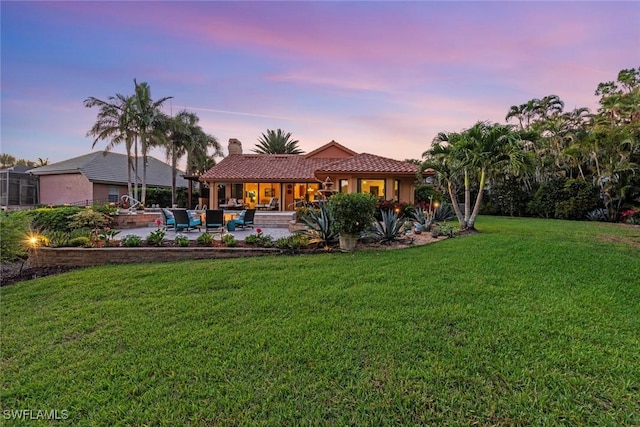 back of house at dusk with a chimney, a yard, a tile roof, a patio, and outdoor lounge area