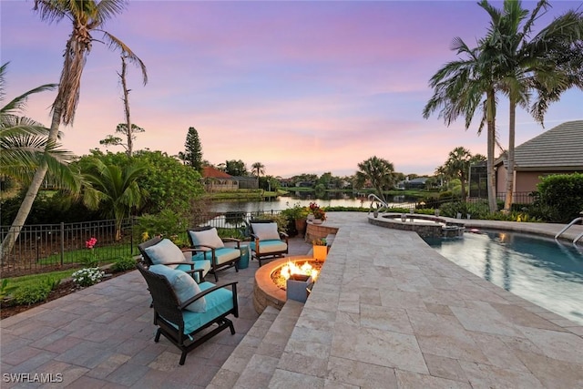 view of pool featuring a fire pit, a water view, a patio area, a pool with connected hot tub, and fence