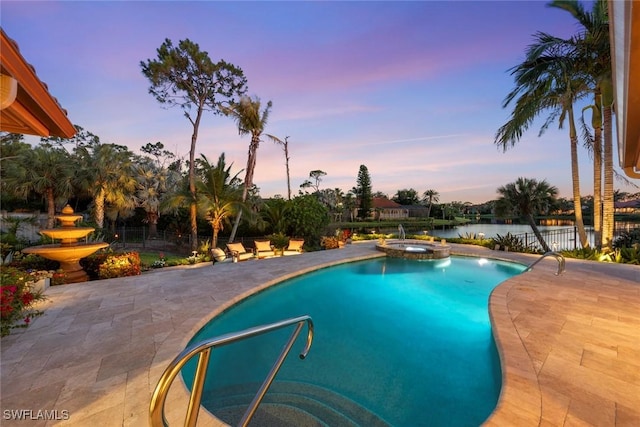 view of pool with fence, a patio, a pool with connected hot tub, and a water view