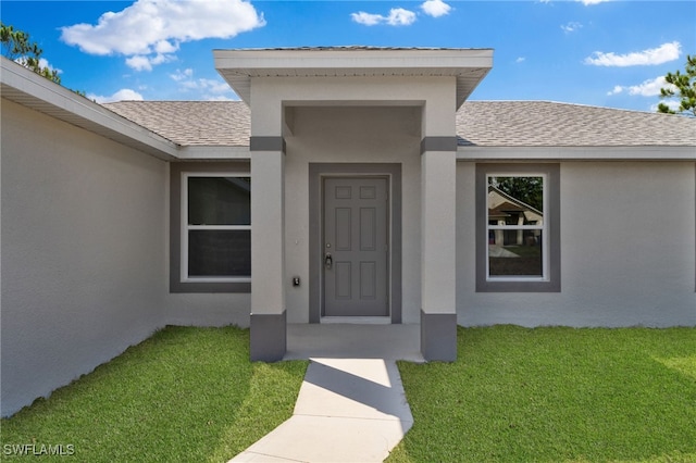 property entrance featuring roof with shingles, stucco siding, and a lawn