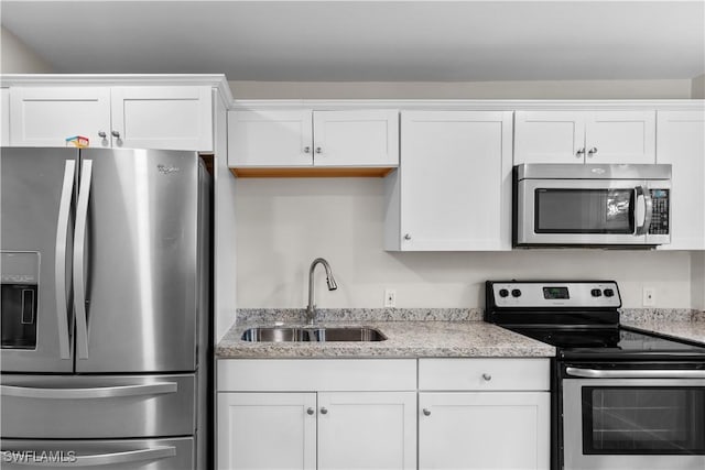 kitchen with appliances with stainless steel finishes, a sink, white cabinets, and light stone counters