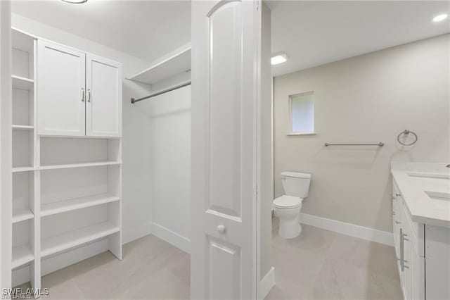 full bath with baseboards, toilet, vanity, and a closet