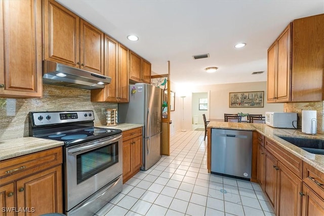 kitchen with stainless steel appliances, under cabinet range hood, brown cabinetry, backsplash, and recessed lighting