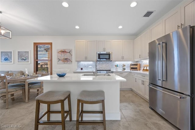 5692 Cassidy Ln, Ave Maria, FL 34142 - kitchen with appliances with stainless steel finishes, light countertops, backsplash, a kitchen bar, and a kitchen island with sink