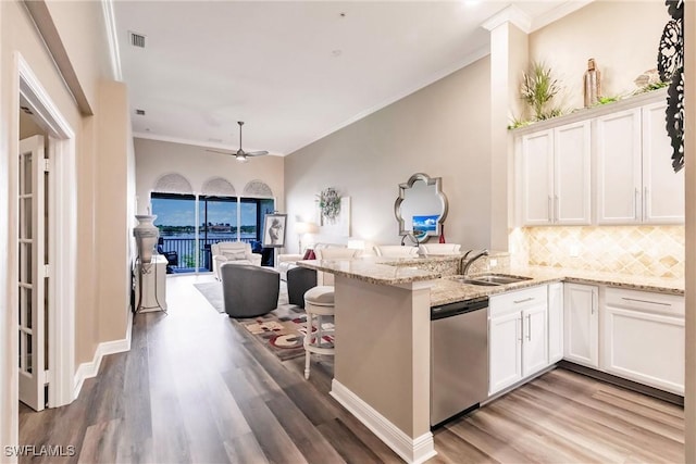 kitchen with stainless steel dishwasher, a sink, open floor plan, a peninsula, and white cabinetry