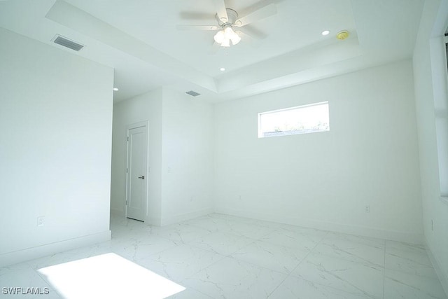 empty room featuring baseboards, ceiling fan, recessed lighting, a tray ceiling, and light marble finish floors