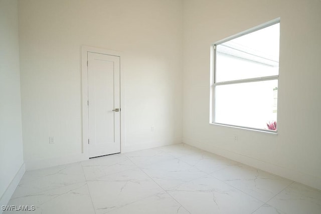 unfurnished room featuring light marble finish flooring and baseboards