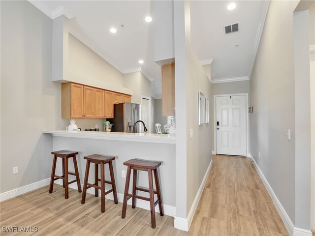19920 Barletta Ln Unit 1423, Estero, FL 33928 - kitchen with stainless steel refrigerator with ice dispenser, ornamental molding, light wood finished floors, a kitchen bar, and light countertops