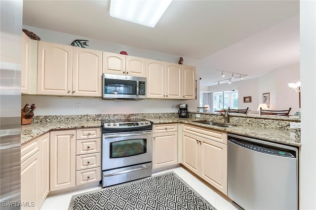 kitchen featuring appliances with stainless steel finishes, a sink, track lighting, and light stone countertops