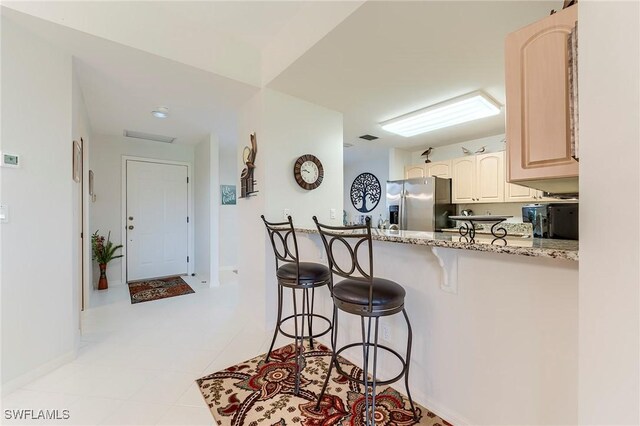 kitchen with stainless steel fridge with ice dispenser, a breakfast bar, light stone countertops, light tile patterned flooring, and baseboards