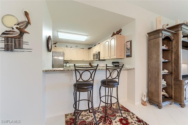 kitchen featuring appliances with stainless steel finishes, a breakfast bar area, baseboards, light tile patterned flooring, and a peninsula