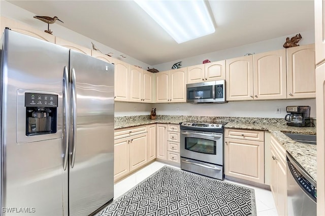 kitchen with stainless steel appliances, light tile patterned floors, and light stone counters