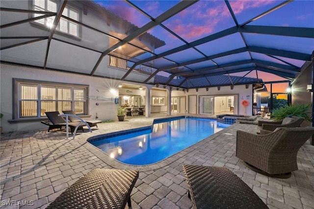 pool at dusk featuring a patio, a pool with connected hot tub, and a lanai