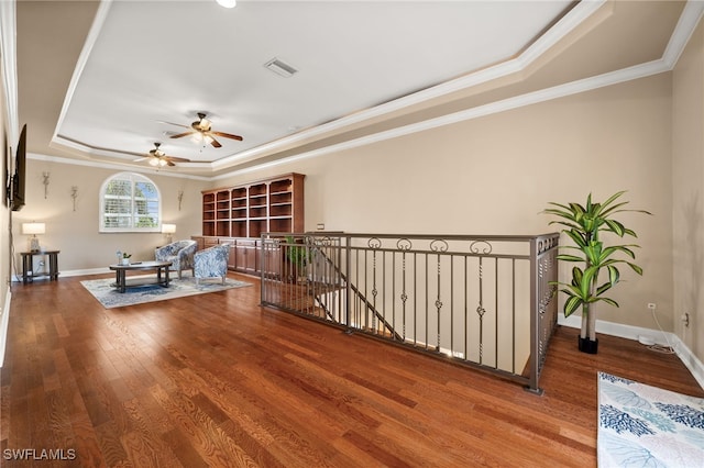 living area featuring a tray ceiling, wood finished floors, a ceiling fan, crown molding, and an upstairs landing