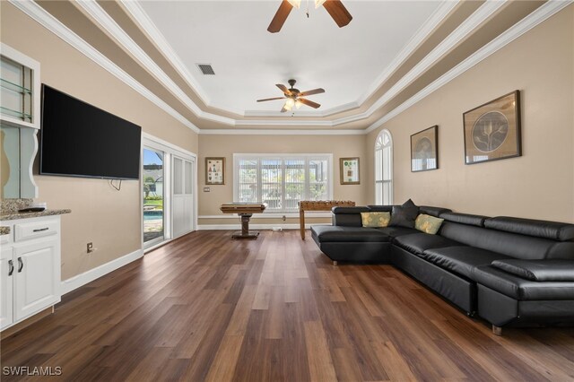 living room with a tray ceiling, a ceiling fan, dark wood-type flooring, ornamental molding, and baseboards