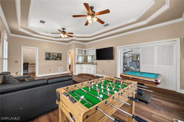 recreation room featuring a raised ceiling, dark wood-type flooring, ceiling fan, healthy amount of natural light, and ornamental molding