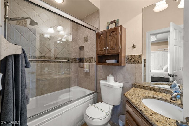 full bathroom with ensuite bath, tile walls, vanity, combined bath / shower with glass door, and toilet
