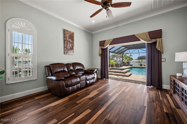 living room featuring ceiling fan, wood finished floors, baseboards, ornamental molding, and a sunroom