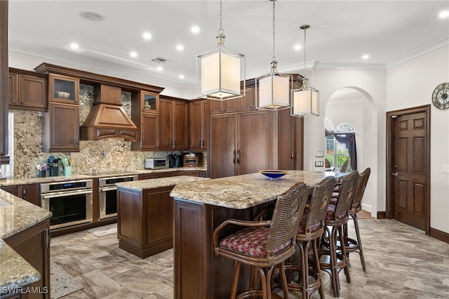 kitchen with a kitchen island, stainless steel oven, custom exhaust hood, arched walkways, and backsplash