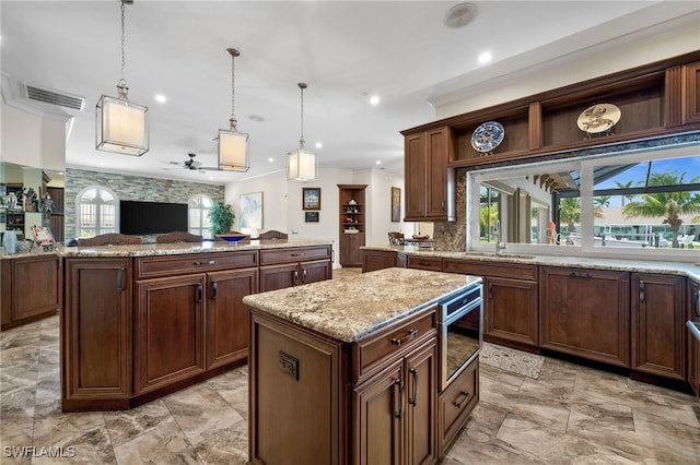 kitchen with a kitchen island, a sink, a ceiling fan, open floor plan, and hanging light fixtures
