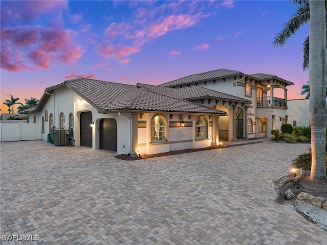 back of house at dusk with an attached garage, stucco siding, fence, a tile roof, and decorative driveway