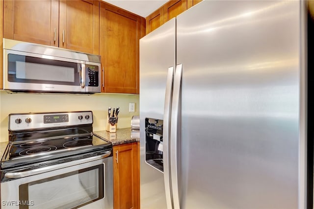kitchen with appliances with stainless steel finishes, brown cabinetry, and dark stone countertops