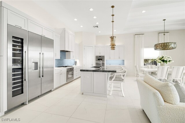 18492 Miromar Lakes Blvd W, Miromar Lakes, FL 33913 - kitchen with white cabinetry, backsplash, gas stovetop, custom exhaust hood, and a breakfast bar