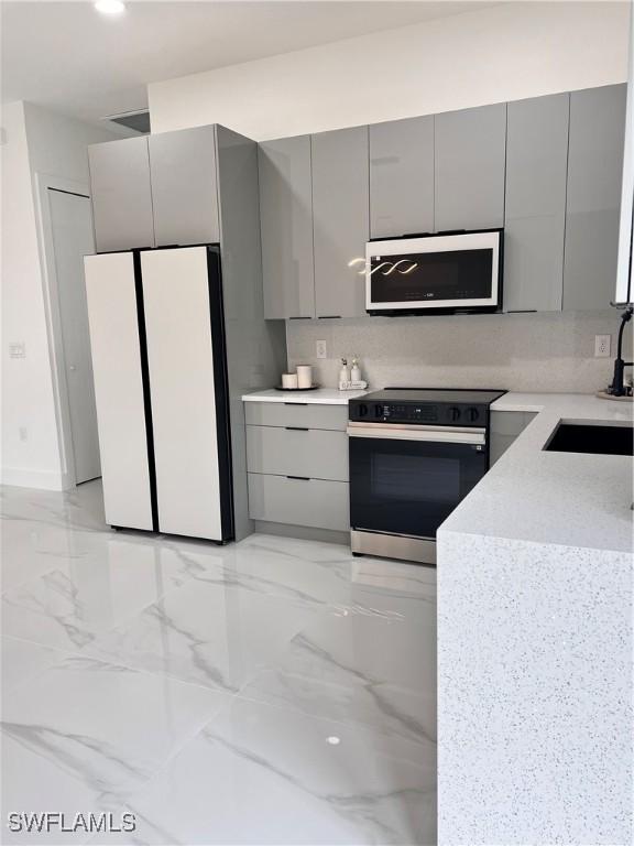 kitchen with white appliances, gray cabinetry, a sink, modern cabinets, and light marble finish floors