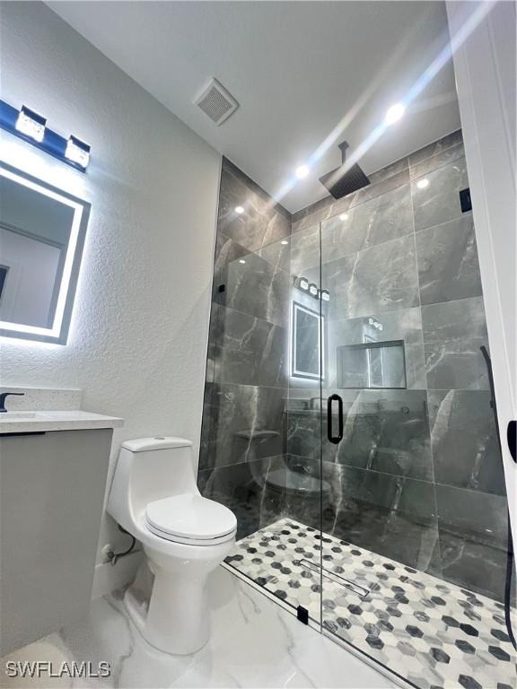 bathroom featuring a stall shower, toilet, vanity, a textured wall, and marble finish flooring