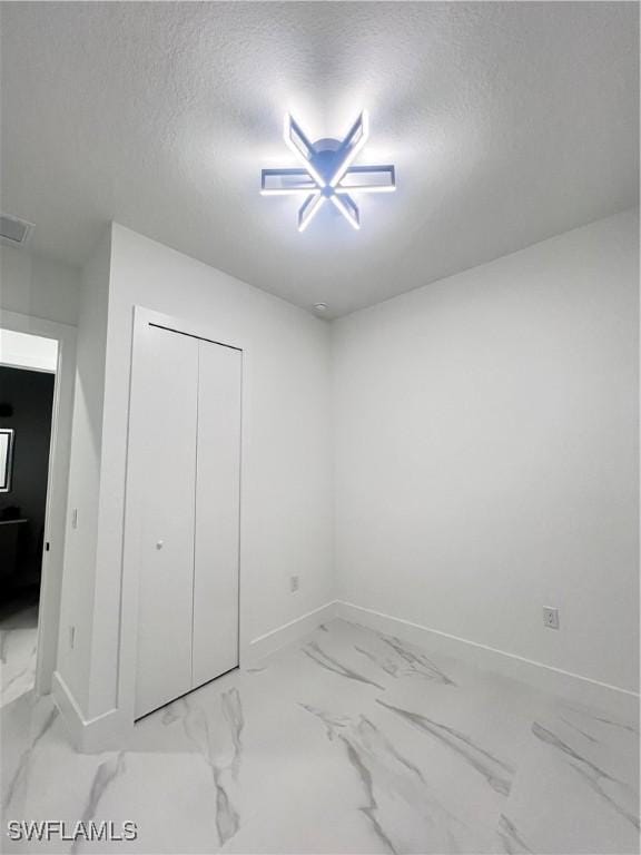 unfurnished bedroom with baseboards, a textured ceiling, marble finish floors, and a closet