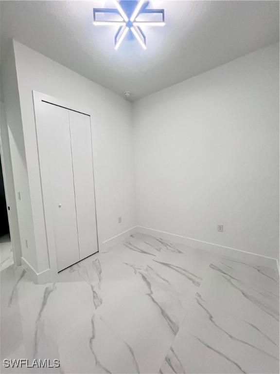 unfurnished bedroom featuring baseboards, light marble finish flooring, and a closet