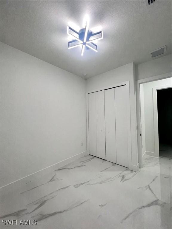 unfurnished bedroom with baseboards, a textured ceiling, light marble finish floors, and a closet