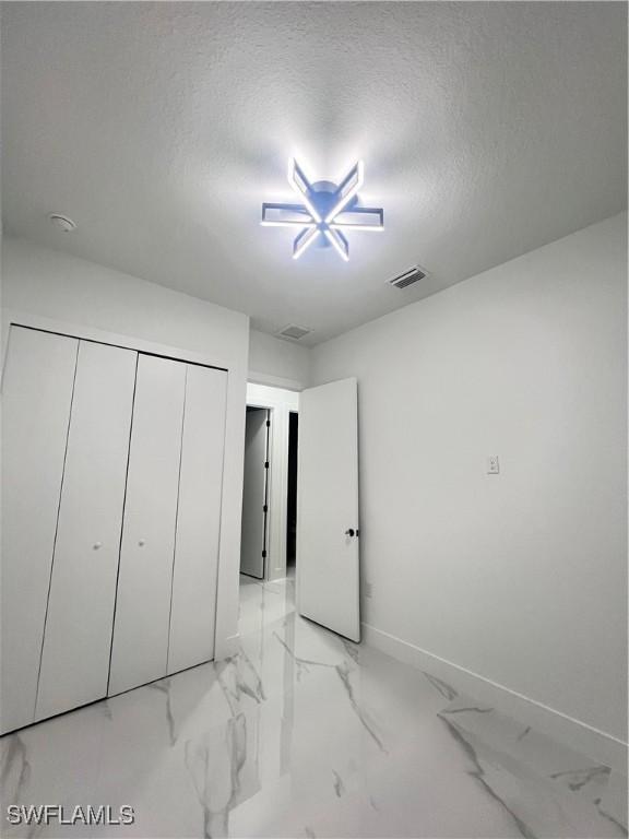 unfurnished bedroom with light marble finish floors, a textured ceiling, baseboards, and a closet