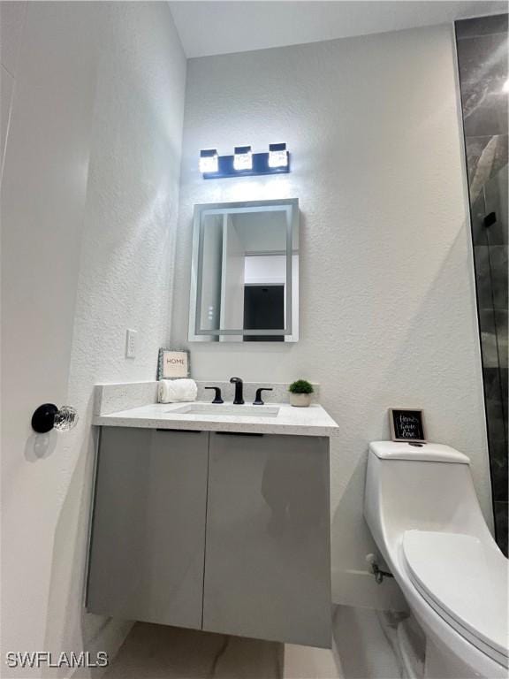 bathroom featuring vanity, toilet, a shower, and a textured wall