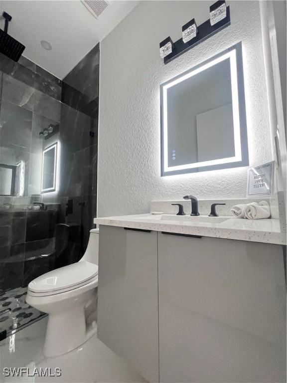 bathroom with a textured wall, toilet, vanity, walk in shower, and marble finish floors