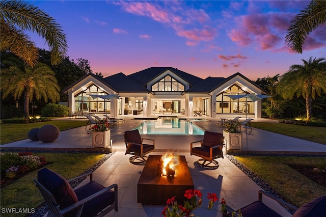 115 E Ave, Naples, FL 34108 - back of property at dusk with an outdoor fire pit, a patio, an outdoor pool, a lawn, and stucco siding