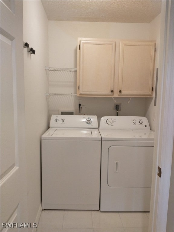 laundry area featuring cabinet space, washer and dryer, light tile patterned floors, and a textured ceiling