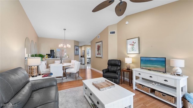 living area featuring a ceiling fan, a chandelier, light wood-type flooring, vaulted ceiling, and baseboards