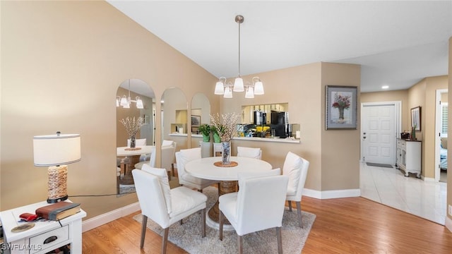 dining room featuring a chandelier, baseboards, light wood-style flooring, and vaulted ceiling