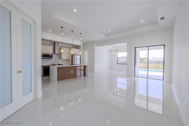 kitchen with stainless steel microwave, wall chimney range hood, freestanding refrigerator, modern cabinets, and a raised ceiling