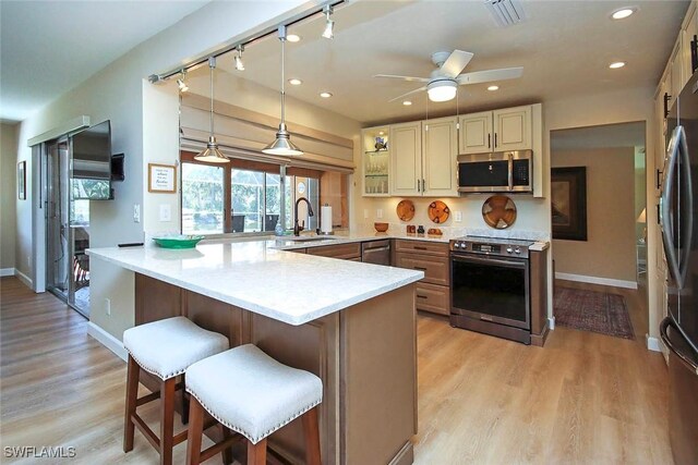 kitchen with appliances with stainless steel finishes, a kitchen breakfast bar, a peninsula, light countertops, and track lighting