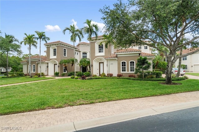 mediterranean / spanish-style house with a tile roof, stucco siding, and a front yard