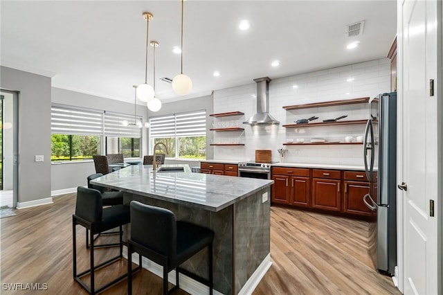 kitchen with stainless steel appliances, a sink, tasteful backsplash, light wood-type flooring, and wall chimney exhaust hood
