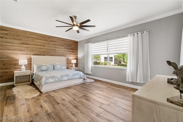 bedroom with ornamental molding, wooden walls, baseboards, wood finished floors, and a ceiling fan