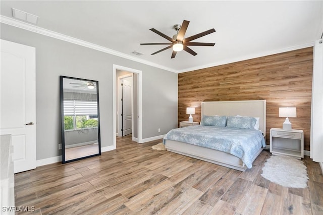 bedroom with baseboards, an accent wall, crown molding, wood finished floors, and ceiling fan