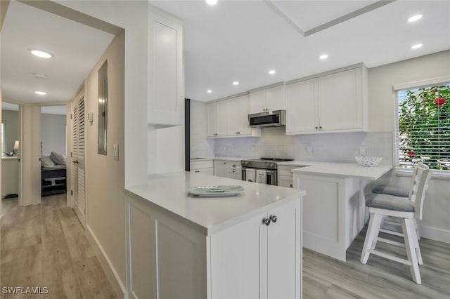 354 Harbour Dr Unit 354, Naples, FL 34103 - kitchen featuring appliances with stainless steel finishes, a peninsula, light countertops, light wood-type flooring, and baseboards